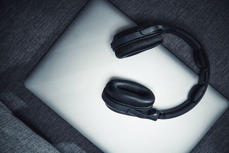 Silver Closed Laptop Computer Sitting On Gray Couch With Big Black Wireless Headphones On Top. の写真素材
