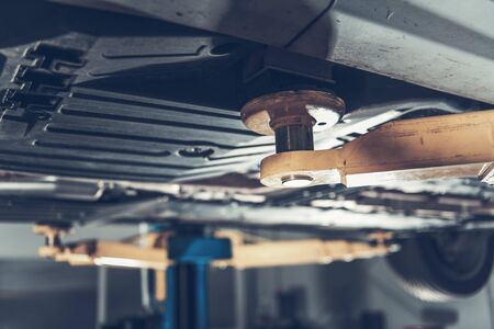 Close Up View Of Under Car Serviced In Garage Being Raised On Hydraulic Vehicle Lift.  の写真素材