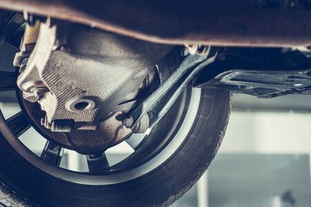 Close Up Of Tire And Bottom Of Car Suspended On Hydraulic Lift Being Serviced At Mechanic. 