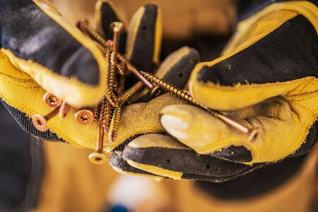 Close Up Of Construction Worker Hands In Gloves Holding Bunch Of Golden Long Screws. の写真素材