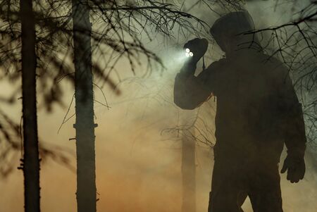 Rescue Search. Men Wearing Camouflage Clothing with Powerful Flashlight Between Trees and Fire Smoke. Forest Wildfire Rescue Mission. の写真素材