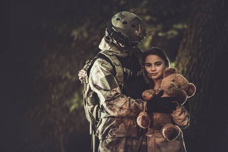 Caucasian Soldier in His 30s in Camouflage Suit Return From Army Mission and Meeting His Daughter. Family Reunited. Girl with Teddy Bear in Hands She Received as Gift From Her Father. Military Theme.の写真素材