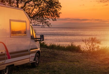 Waterfront RV Camping Site. Camper Van Road Travel. Scenic Sunset in Calm Sea Front Place. Recreational Vehicles Theme. Travel Industry.の写真素材