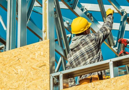 Contractor Worker in Yellow Hard Hat Head Protection on a Construction Site. Residential Building Skeleton Steel Structureの写真素材