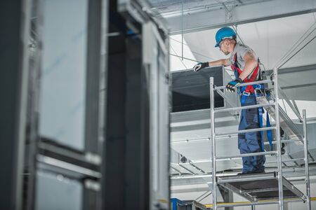 Construction Worker Checking Newly Installed Air Ventilation Shaft On Ceiling Of Large Commercial Building.の写真素材