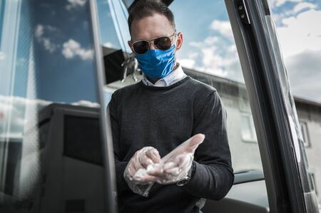 Caucasian Coach Bus Driver With Protective Face Mask Putting On Gloves And Getting Ready For Work During Pandemic.の写真素材