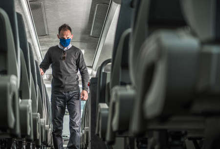 Public Transportation Passenger in Face Mask Walking Along Coach Bus Alley Looking For Safety Seat...