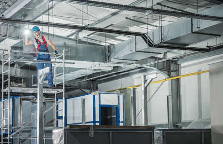Professional HVAC Technician with Flashlight Overlooking Finished Air Ventilation System in the...