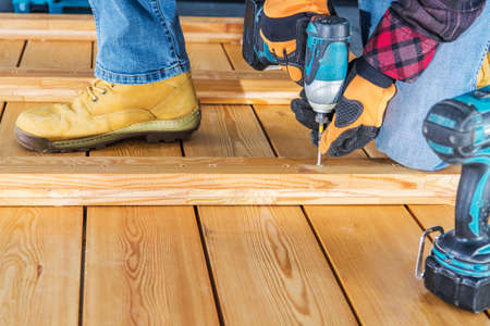 Caucasian Worker Assembling Wood Boards Using Cordless Drill Driver to Build Wooden Wall