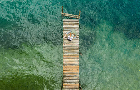 Caucasian Men Working on His Laptop While on Vacation. Computer Remote Work on Wooden Pier Aerial View.の写真素材