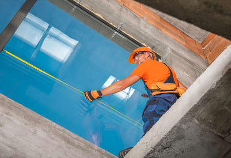 Caucasian Windows Technician Finishing Commercial Building Large Format Aluminium Window Installation. Final Measuring. Construction Industry Theme.の写真素材