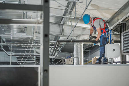 Caucasian HVAC Technician in His 40s Finishing System Assembly Inside Commercial Building Warehouse....
