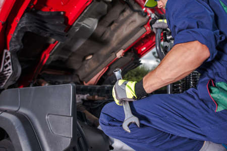 Caucasian Semi Trucks Mechanic with Large Wrench in His Hand Looking Inside Truck Vehicle Engine...
