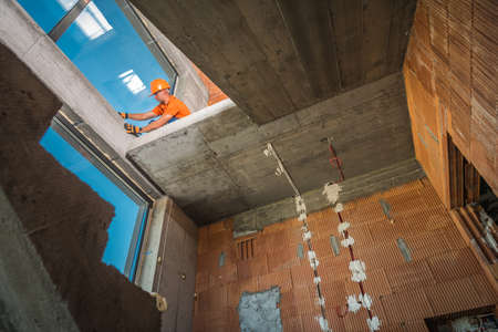 Caucasian Construction Site Worker Wearing Hard Hat Finishing Building Stairs Elements. Concrete Blocks Made Building Staircase. Industrial Theme.の写真素材