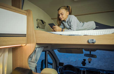 Caucasian Girl Hanging on Bunk Camper Bed with Her Smartphone During Camping Time and Rainy Weather....
