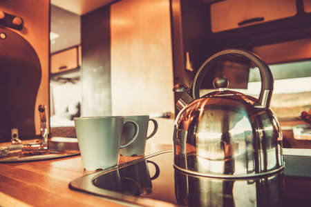 Shiny Metal Water Kettle and Two Cups with Hot Tea Inside RV Camper Van Kitchen Area. Recreational Vehicle Getaway Theme.の写真素材