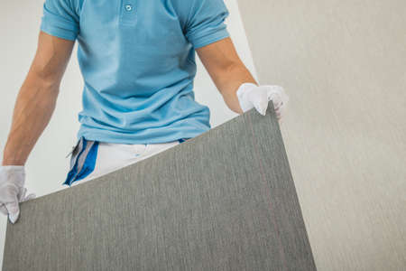 Caucasian Men in His 40s Preparing New Vinyl Wallpaper for Wallcover Inside Clean White Room...