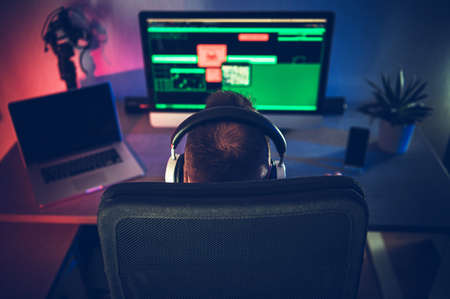 Caucasian Men in His 40s Wearing Headphones in Front of His Desktop Office Computer. Chair Rear View. Modern Technologies and Home Office Work.の写真素材