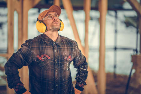 Construction Contractor in His 40s Wearing Noise Reduction Headphones and Eyes Protection Glasses...