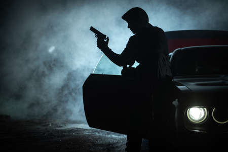 Caucasian Pensive Gangster in His 40s Playing with His Handgun During Late Night. Seating on His Car...