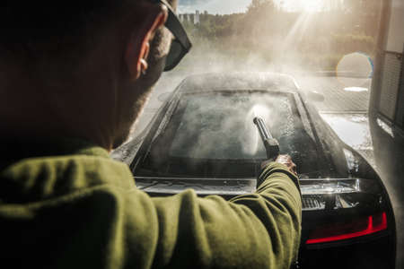 Caucasian Exotic Car Owner in His 40s Pressure Washing His Sporty Car Using Pressured Water Flow. Car Maintenance Theme.の写真素材