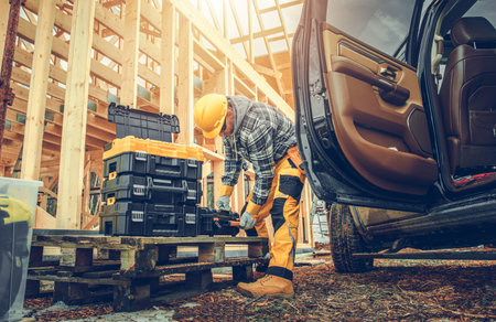 Caucasian Construction Contractor in His 40s Preparing His Tools Next To Pickup Truck and Wooden Skeleton Frame of Newly Building Home. Industrial Theme.の写真素材