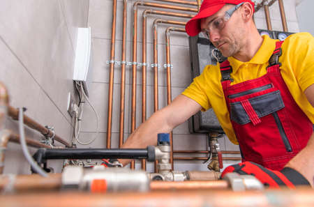 Caucasian Residential Heating Systems Technician in His 40s at Work. Hot and Cold Water Copper Made Pipelines in a Background.の写真素材