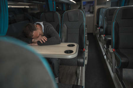 Tired Caucasian Businessman Sleeping on Coach Bus Table While in Business Travel.の写真素材