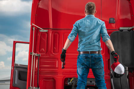 Surprised Caucasian Semi Trucker in His 30s Staying on Fifth Wheel of His Truck and Looking on Cabin Elements. Transportation Theme.の写真素材