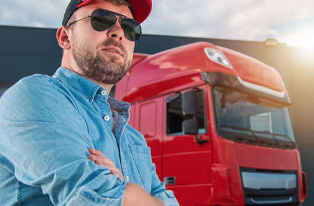 Caucasian Semi Truck Driver in His 30s Portrait in Front of His Tractor Truck. Heavy Duty...