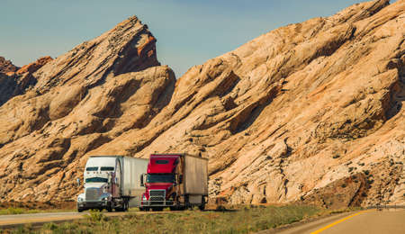 Two Speeding Semi Trucks on Interstate 70 Highway in Scenic Utah Landscape. Heavy Duty American...