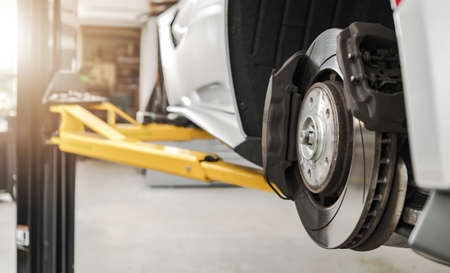 Modern Vehicle Braking Discs and Pads Replacing in Authorized Auto Service Close Up. Car on a Lift...