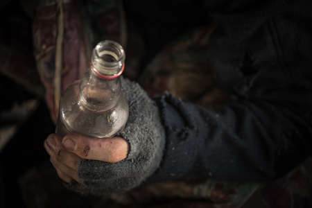 Caucasian Homeless Men Wearing Fingerless Gloves with a Bottle of Vodka Close Up.の写真素材