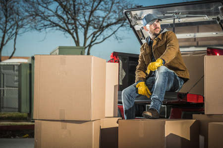 Caucasian Courier in His 40s with Shipping Boxes Parcels Taking Short Break Seating on His Pickup Truck. Unloading Cargo.の写真素材