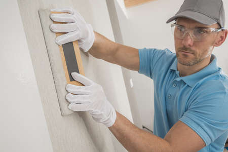 Caucasian Worker with Clean White Gloves and Soft Wooden Vinyl Squeegee Applying Modern Vinyl Wallpaper.の写真素材