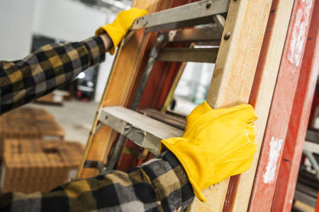 Construction Worker Wearing Safety Gloves Moving Commercial Grade Ladders Within Construction Site.の写真素材