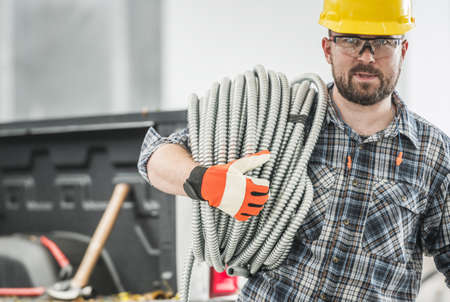 Caucasian Professional Contractor with Conduit Electric Pipe on His Shoulder. Men Wearing Eyes...