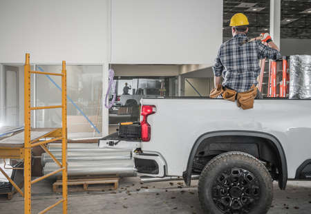 Caucasian Construction Contractor Worker with Large Hummer Taking Short Work Brake Seating on His Pickup Truck Cargo Bed Side.の写真素材