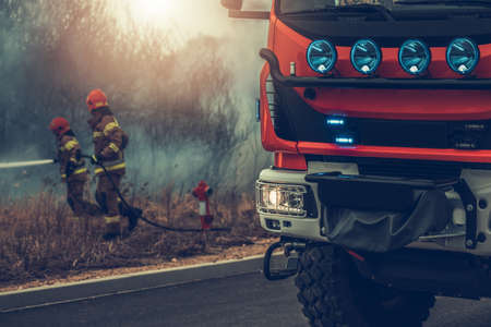 Modern European Fire Truck and Two Firefighters Fighting Grass Wildfire in Backgroundの写真素材