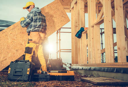 Caucasian Construction Industry Worker in His 40s Moving Plywood Elements. Wooden Skeleton House...