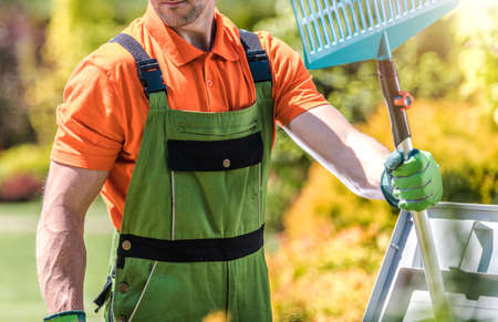 Caucasian Men in His 40s with Plastic Rake in His Hand. Backyard Garden Spring Time Maintenance Theme.の写真素材