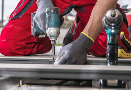 Construction Worker Installing Composite Patio Deck Floor Attaching Elements Using Cordless Drill...