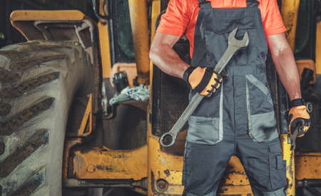 Heavy Construction Equipment Mechanic with Large Wrench in His Hand Staying in Front of Construction...