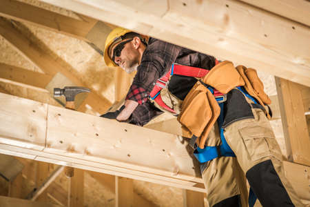 Professional Caucasian Carpenter Assembling Wooden Skeleton Frame of a Building Roof. Wearing Safety...