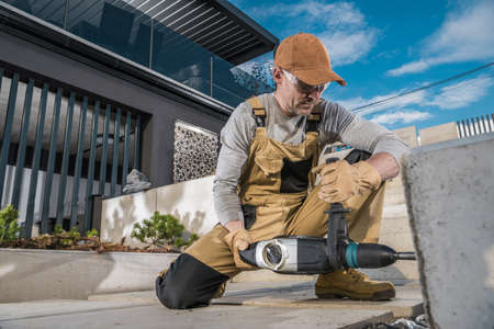 Caucasian Landscaper Drilling Holes Using Professional Cordless Driller Inside Concrete Backyard Elements For LED Lighting Installation. Outdoor Stairs Illumination.の写真素材