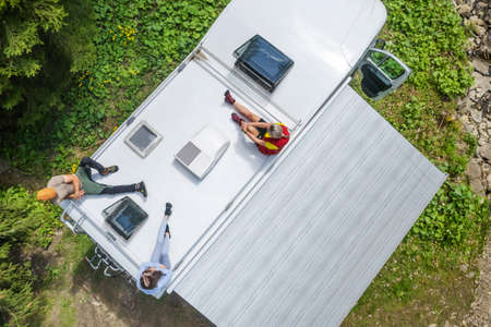 Caucasian Family Chilling Out on a Top of Their Camper Van Motorhome Enjoying Summer Vacation Sun....