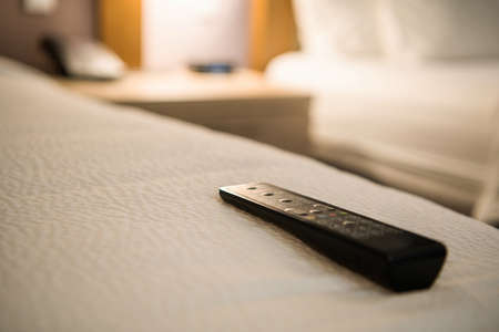 Hotel Television Remote on a Bed. Satellite Channels Watching During Business Trip. Travel Theme.の写真素材
