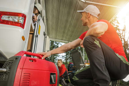 Caucasian Family Camping in Their Camper Van During Vacation Road Trip. Father Preparing Portable Electricity Generator to Connect Motorhome.の写真素材
