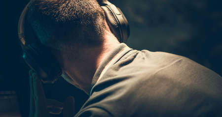 Caucasian Men Listening Music Using Wireless Headphones Inside a Dark Room.の写真素材