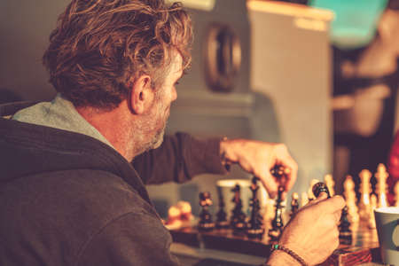 Caucasian Male in His 40s Playing Chess with His Wife in Front His RV. Setting Sun Casts His Shadow...